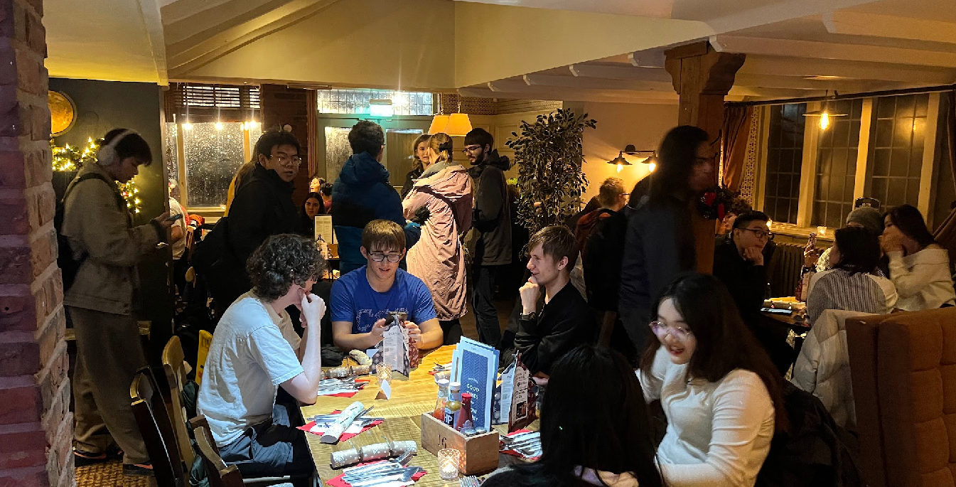 A picture of members at the Christmas Meal in the Green Man, some students sitting at tables.